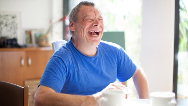 laughing man wearing a blue shirt sitting at a table