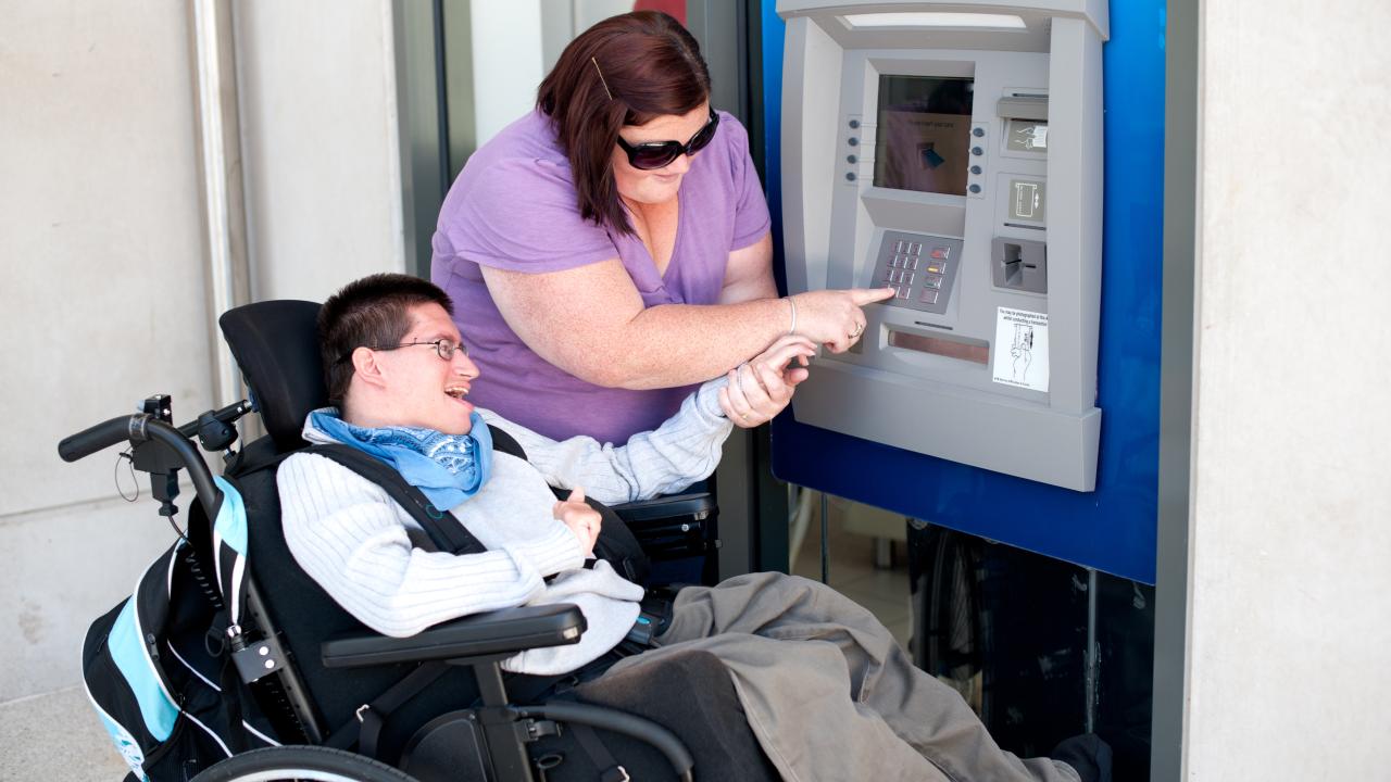 Woman helping a man with developmental disabilities use an ATM machine
