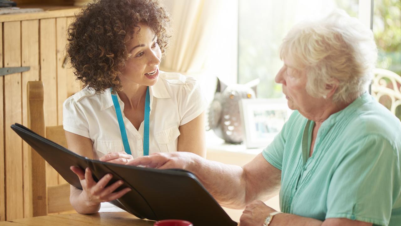 Young woman and elderly woman sitting in her living room looking at paperwork