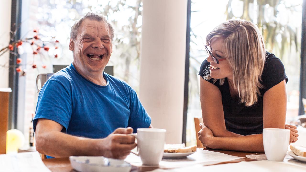 A happy man with Down syndrome sitting next to his caregiver