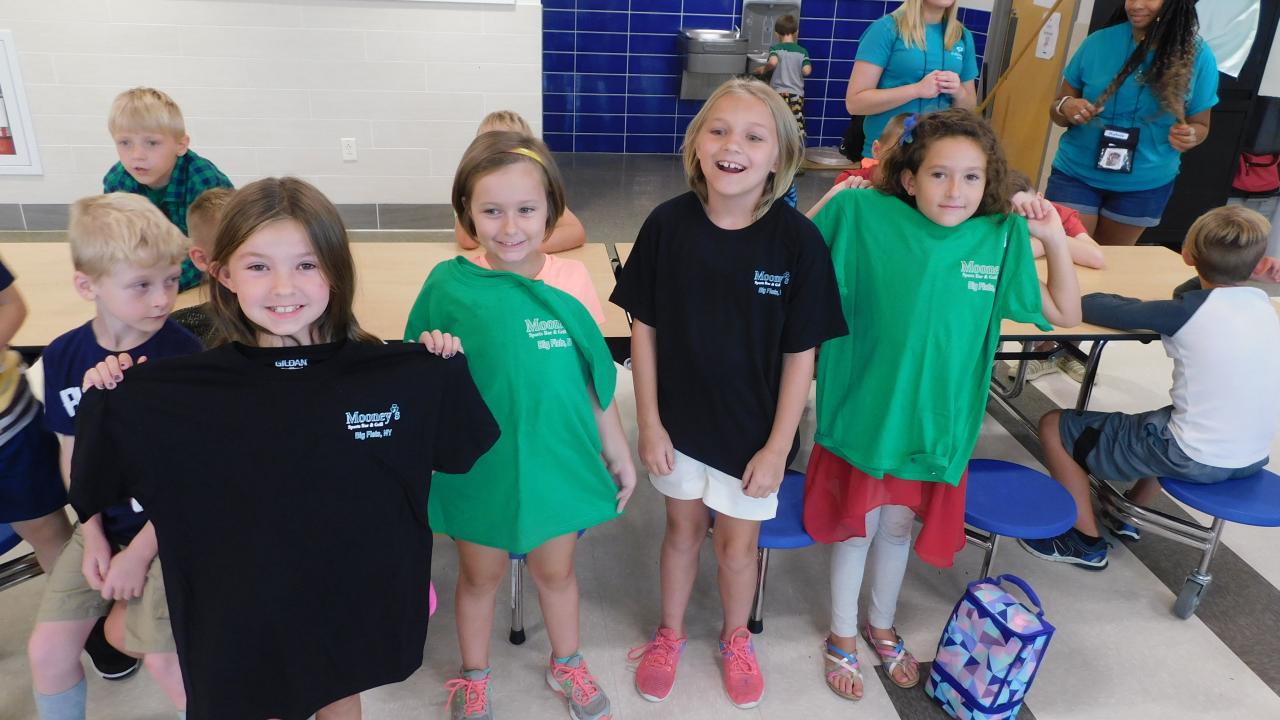 Smiling children holding up t-shirts that they won
