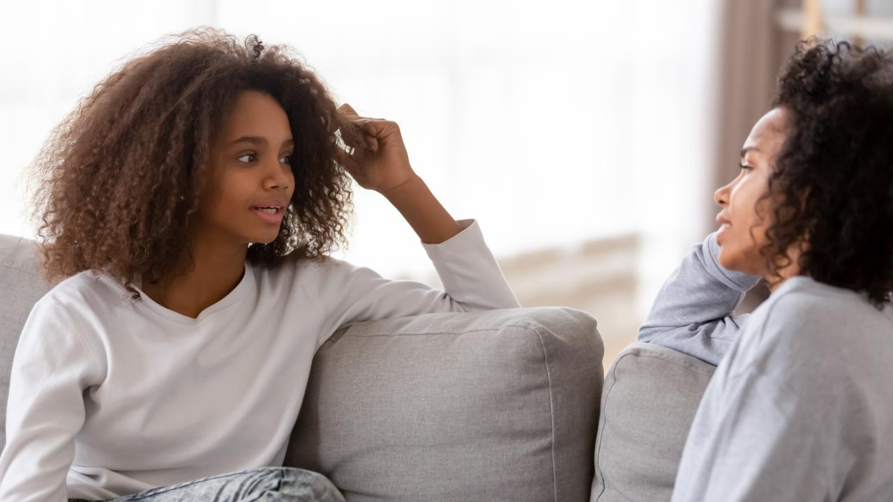 Young girl sitting on a couch talking to a woman