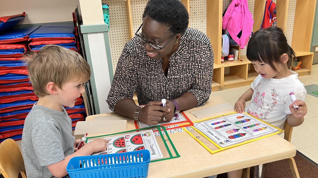Teacher sitting at a table with two small children working on an activity.