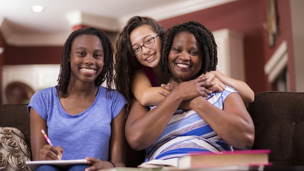 young girl hugging a woman sitting on a couch next to another young girl