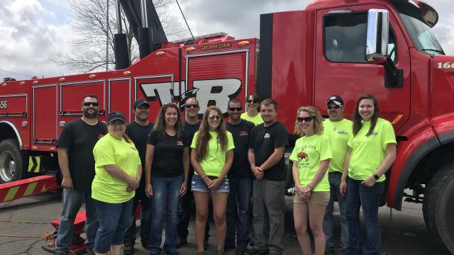 A group of people standing in front a T&amp;R Towing truck