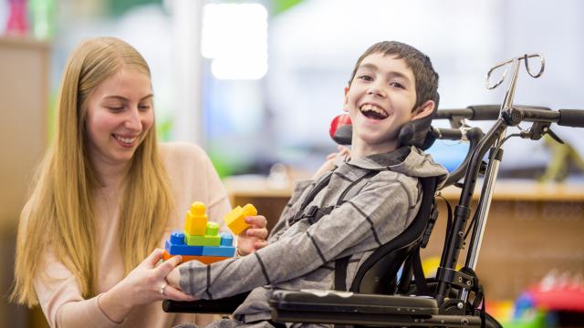 A young boy in a wheelchair having fun with his teacher