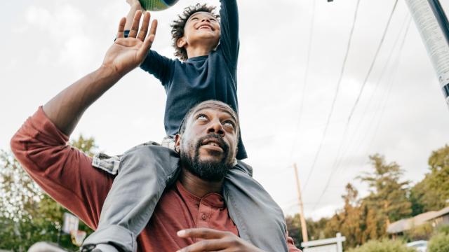 Young boy sitting on the shoulders of a man tossing a basketball